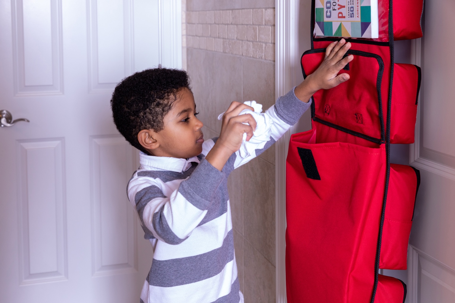 Child choosing clothing from a red SuitcaseMate hanging on a door